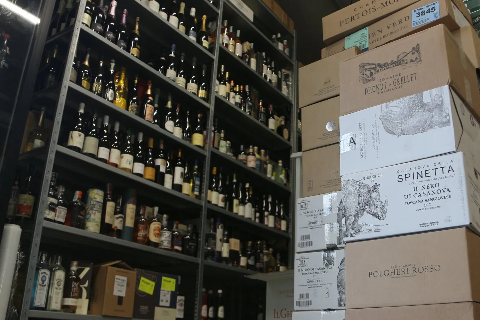 La cantina: scaffali pieni di bottiglie e cartoni di Bolgheri Rosso, Spinetta e Champagne